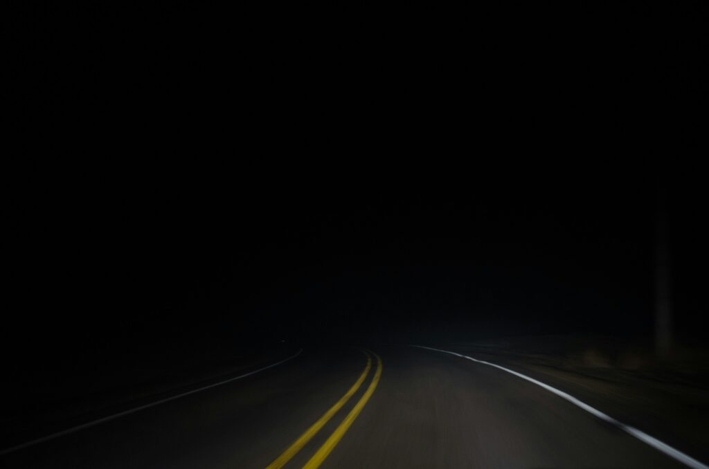 A section of a road in the dark and complete darkness in the background.